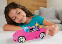 Young girl playing with a toy pink car and dolls on a light-colored surface.